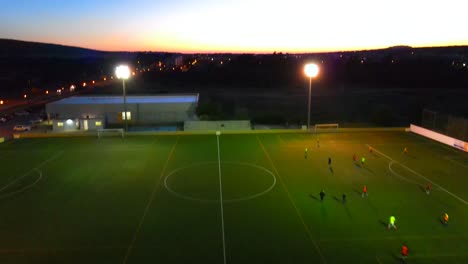 revealing shot of a football field at dusk where people are playing under lights at santa ponsa, mallorca, spain