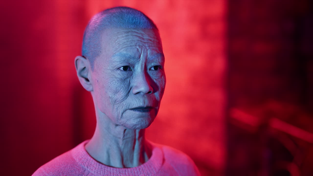 retrato de cerca de una mujer asiática mayor con la cabeza afeitada mirando hacia otro lado