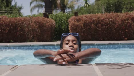 portrait of happy african american girl wearing sunglasses in swimming pool, slow motion