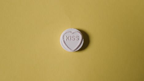 mano recogiendo caramelos de corazón con beso de palabra sobre fondo amarillo