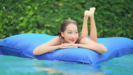 close up of a pretty young woman floating on a huge blue float in the middle of a luxury resort pool