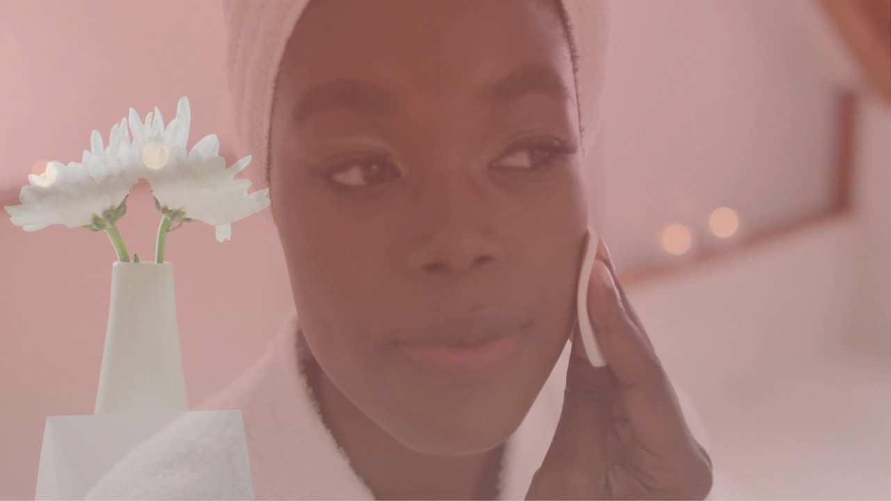 Animasjon av hvite blomster i vase over en glad afroamerikansk kvinne som renser ansiktet på badet