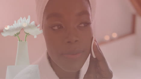 animation of white flowers in vase over happy african american woman cleansing face in bathroom