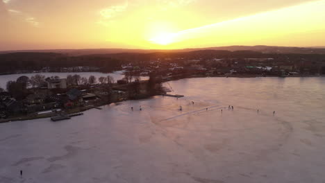 aéreo: volando muy alto sobre el lago congelado con el sol proyectando luz naranja en el hielo