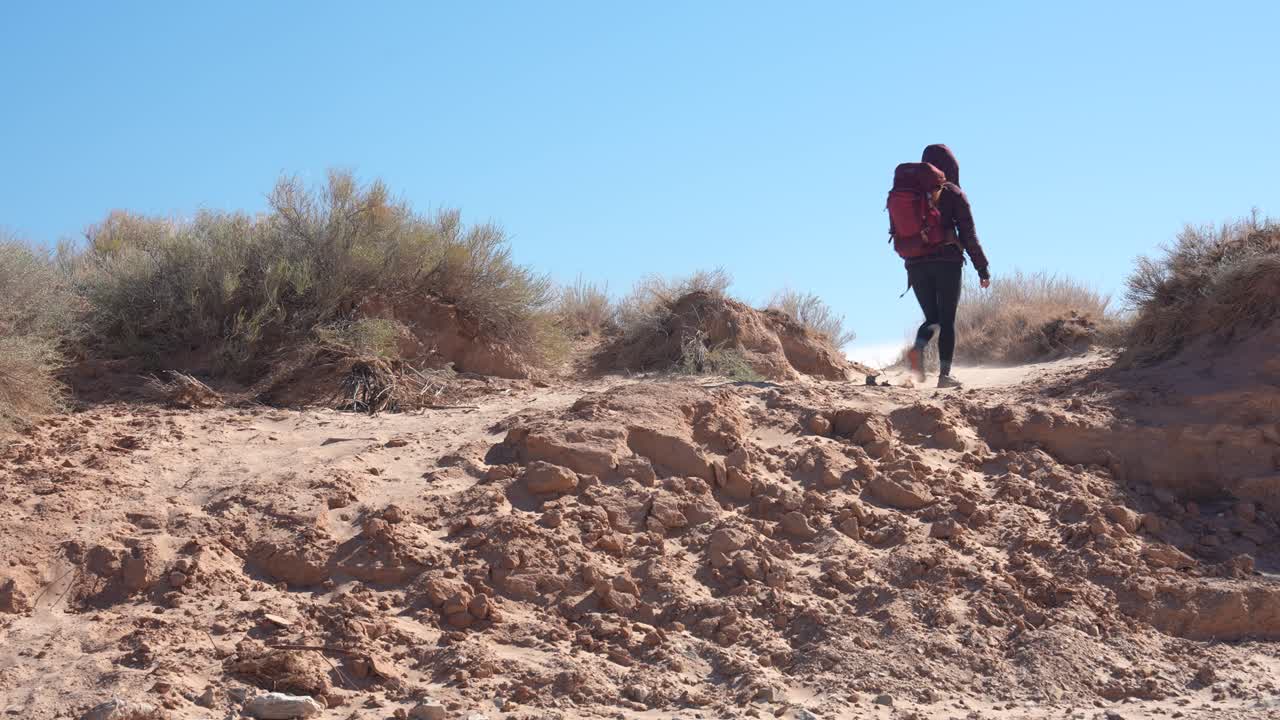 Mulher com mochila caminhando em paisagem desértica em dia ensolarado