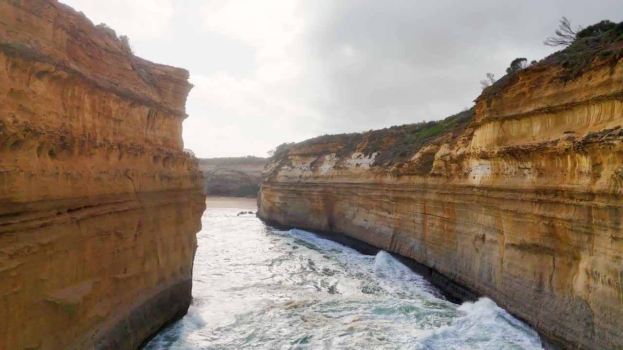 Aerial footage of rugged cliffs and turbulent ocean waves at Loch Ard Gorge, Port Campbell, with overcast skies and dynamic lighting