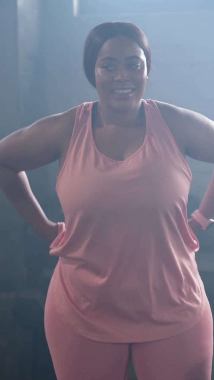 Video verticale: Donna che inizia l'allenamento in palestra, cammina in rosa, tocca lo smartwatch e tiene una bottiglia.