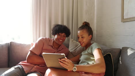 diverse couple relaxing on sofa, smiling while watching tablet together at home