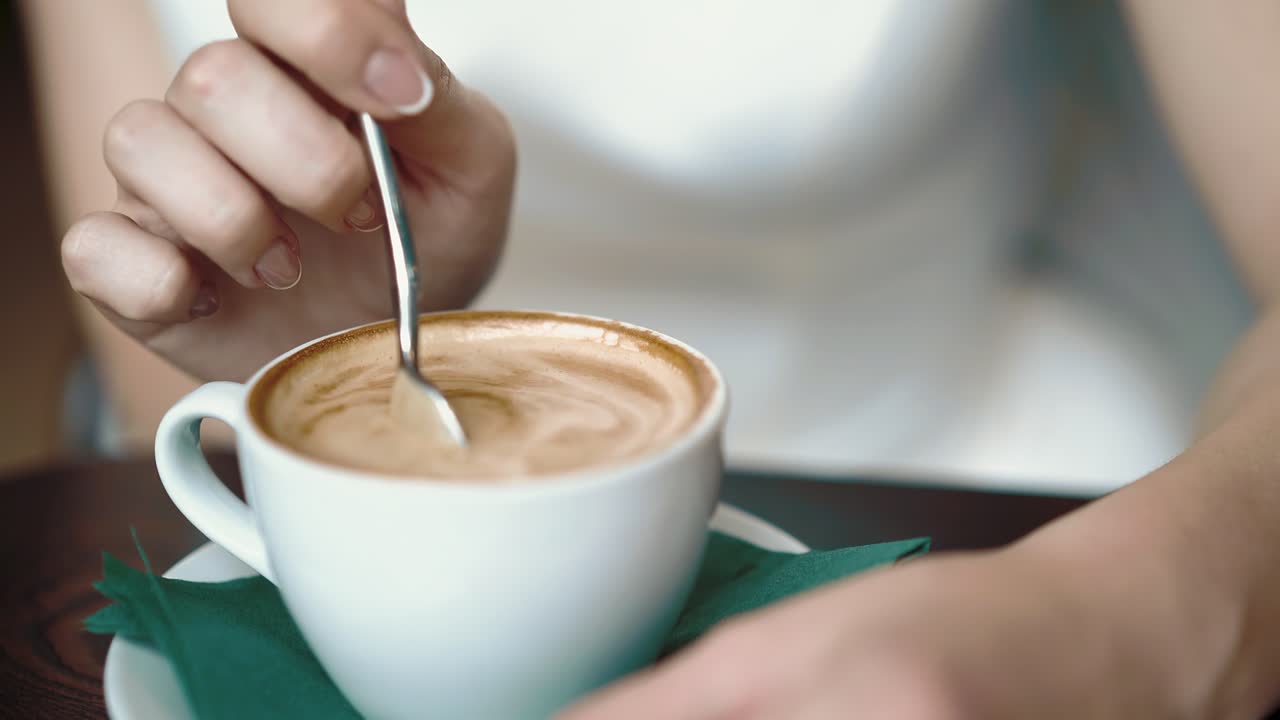 Girl stirs coffee with a spoon dripping drops close-up slow motion