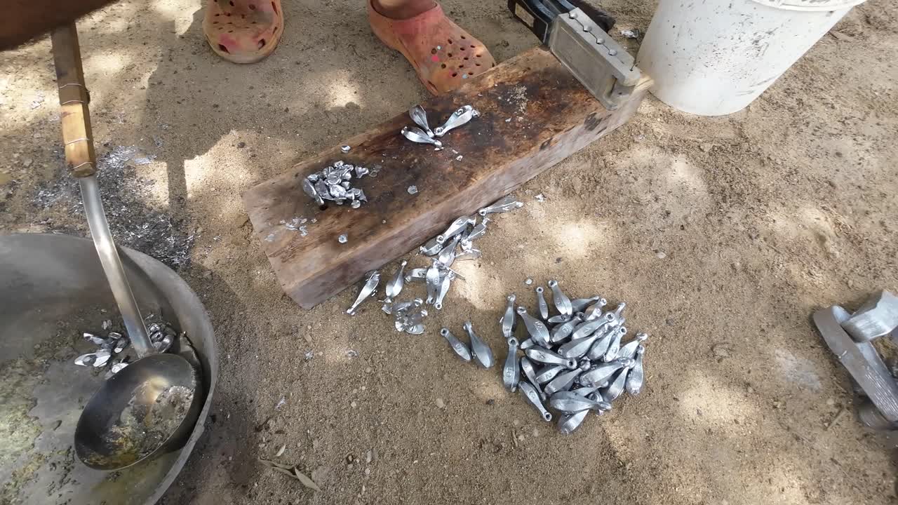 Person creating fishing sinkers using a lead mold outdoors, sand underfoot, hands in focus