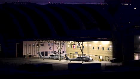 dos helicópteros estacionados en un hangar por la noche.