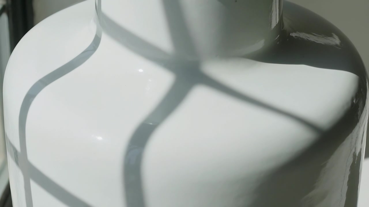 Bevægeligt sollys kaster gitterformet skygge over blank keramisk genstand i to niveauer ved vinduet, med højdepunkter.