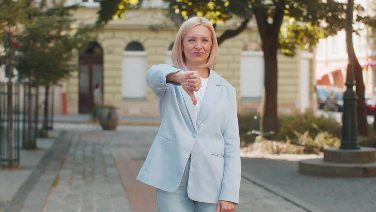 Upset mature caucasian blonde businesswoman in formal suit looking camera and showing thumb down