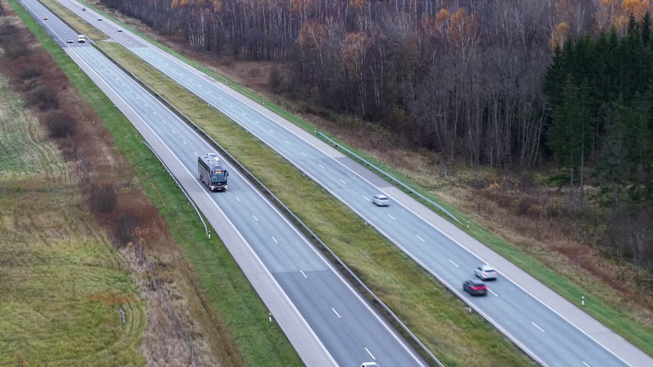 Aerial tracking shot of multiple vehicles speeding down a rural highway. Cars passing by bus on the left side of the lane