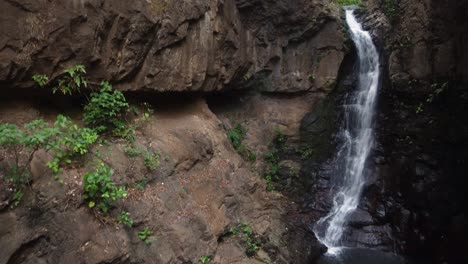 Crane-shot-rises-up-narrow-rock-canyon,-small-tropical-waterfall