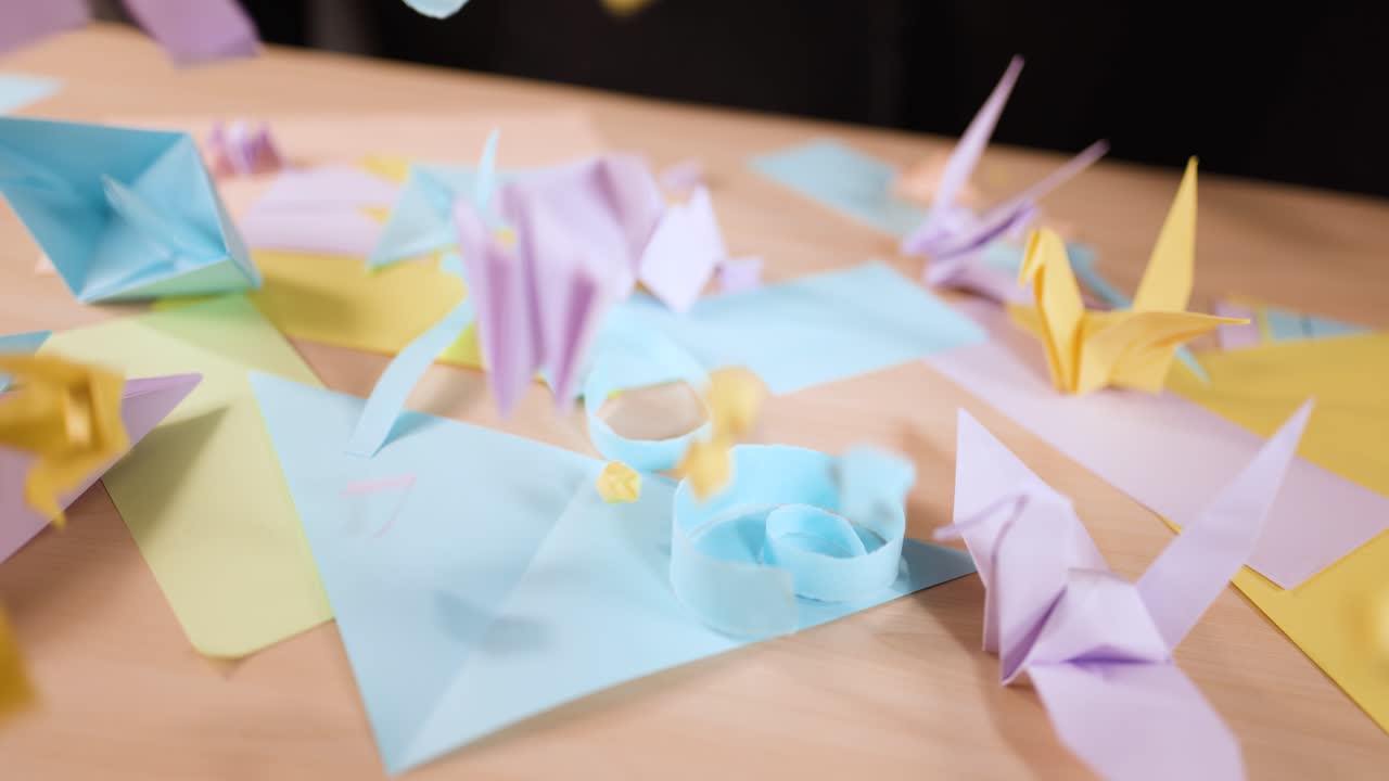 Ripresa al rallentatore di gru e forme origami di carta colorata che cadono su una superficie di legno