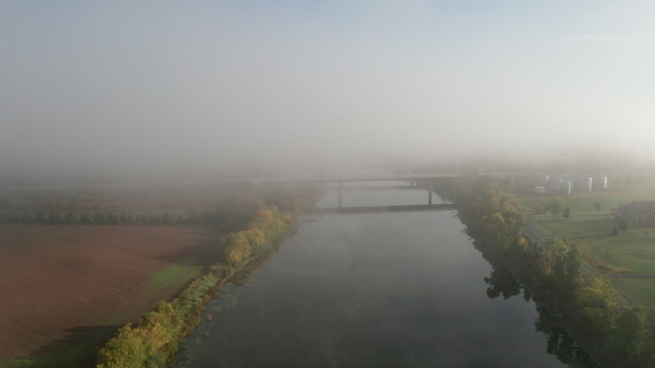 고속도로 다리를 향해 날아다니는 드론은 주변을 반영하는 부드러운 평평한 표면으로 강을 통과합니다.