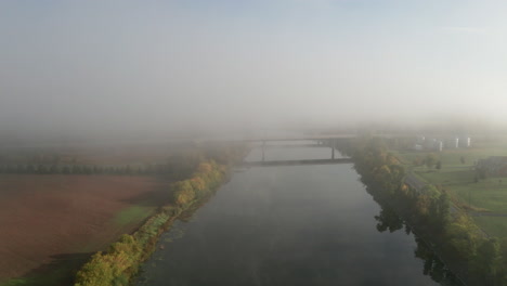 drone flying toward highway bridge over river with smooth flat surface reflecting surroundings