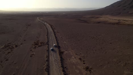 Aerial-view-of-car-overtaking-on-the-dusty-desert-road-at-late-sunset