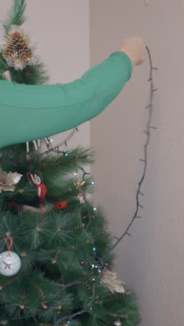 person decorating a christmas tree with lights and ornaments