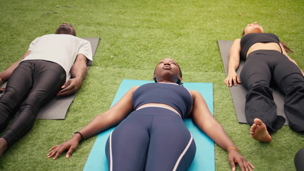 Adults lying flat on yoga mats with arms relaxed beside bodies