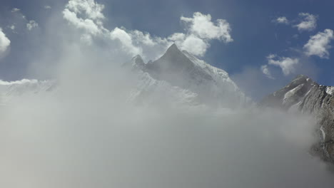 toma aérea épica de un dron de un pico nevado de las montañas annapurna, comenzando en las nubes y luego revelando las montañas en nepal