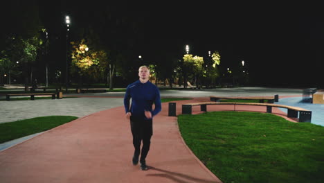 focused blond man running towards camera in the park at night 1