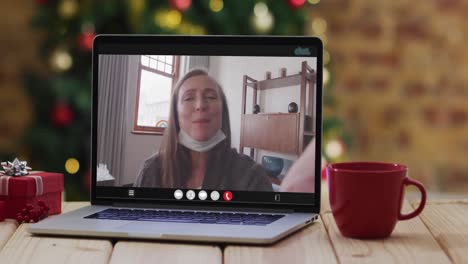 Caucasian-senior-woman-in-face-mask-on-video-call-on-laptop,-with-christmas-tree