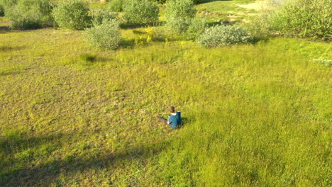 drone slowly circling a teenage boy sitting in the grass, being occupied with his phone