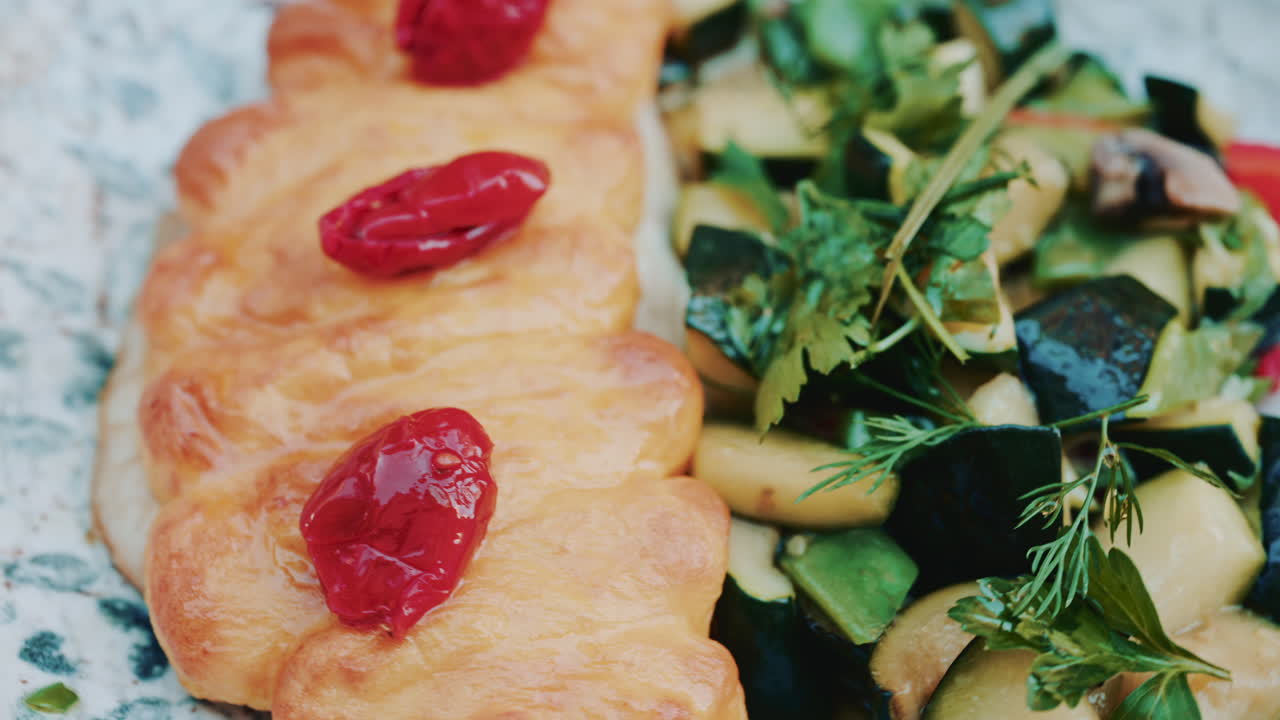 Close up of a golden croissant served with sauteed vegetables and fresh herbs