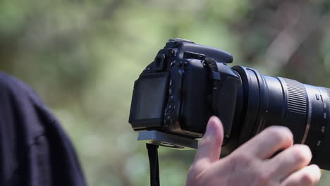 close up: right hand adjusts settings on long lens camera on tripod