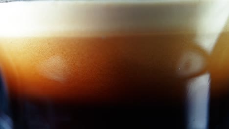 creamy brown coffee dripping to fill the clear glass - macro shot