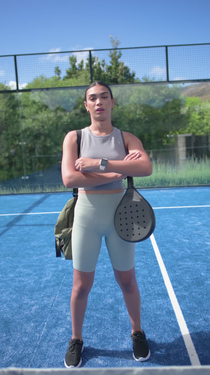 Video vertical: Mujer afroamericana escaneando la cancha azul, revisando la pala, ajustando la mochila y preparándose.