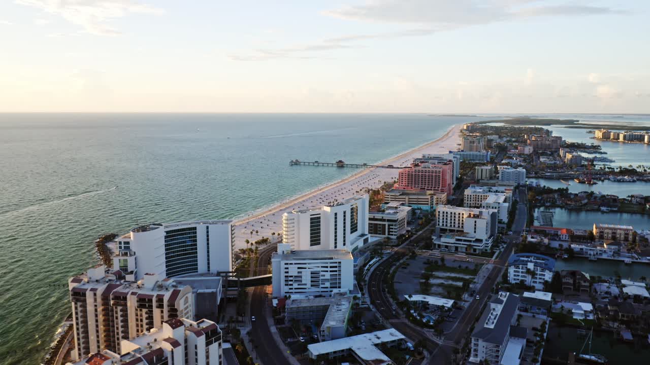 Resorts line the soft white sands of Clearwater Beach as the shoreline stretches toward the pier, framed by the turquoise waters of the Gulf of Mexico