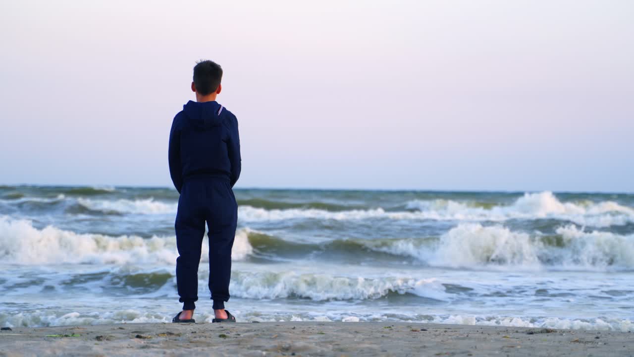 Boy standing on the beach. Rear view of standing boy near sea