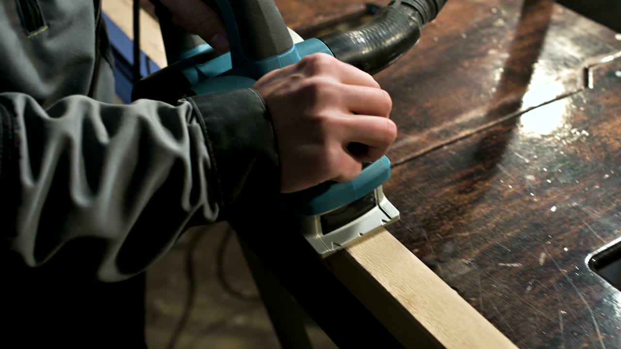 primer plano de la mano de un carpintero trabajando con un avión eléctrico en un taller doméstico