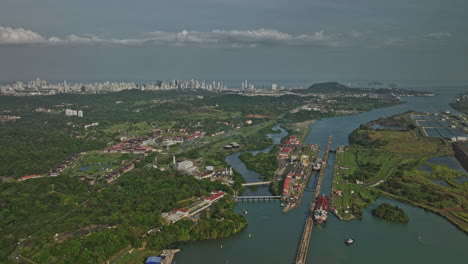 Panama-City-Aerial-V38-Absteigende-Überführung-über-Den-Miraflores-See,-Der-Frachtschiffe-Erfasst,-Die-Am-Schleusenkanal-Vorbeifahren,-Mit-Stadtbild-Im-Fernen-Hintergrund-Entlang-Der-Skyline-–-Aufgenommen-Mit-Mavic-3-Cine-–-März-2022