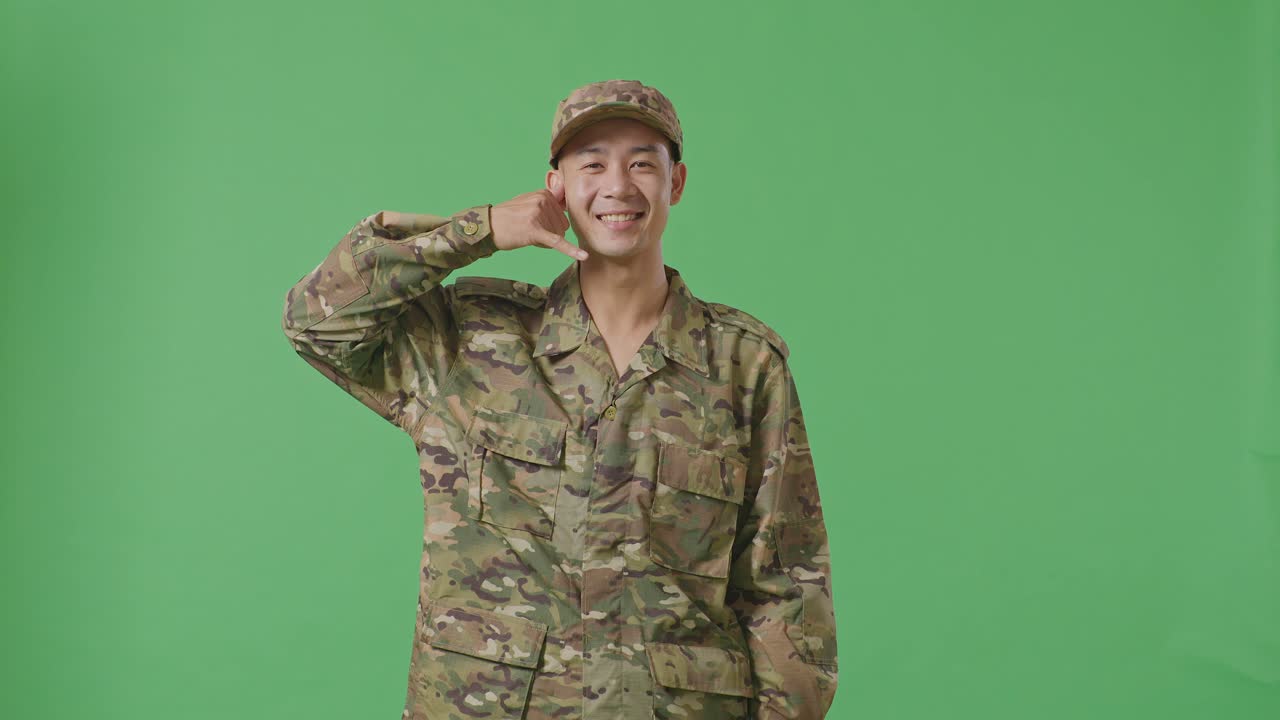 Asian Man Soldier Smiling And Making Call Me Gesture To Camera While Standing In The Green Screen Background Studio