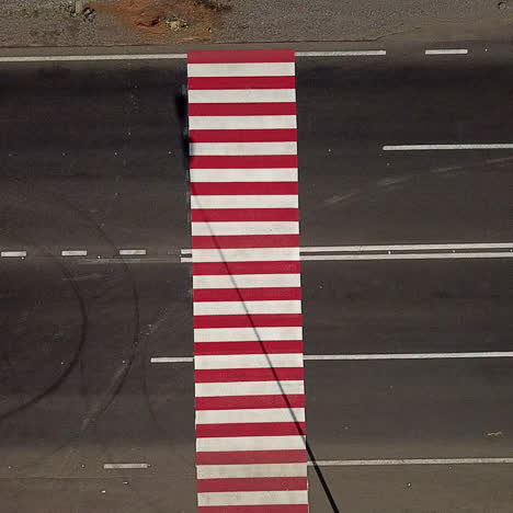 truck is passing through the crossing with red and white stripes painted on black asphalt. top view of crosswalk for pedestrians in the road at daytime. aerial view