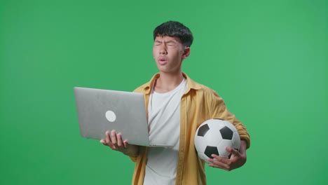 adolescente mirando una computadora portátil con una pelota de fútbol