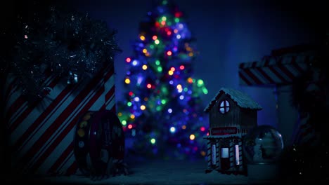 camera slowing pushes towards a little, cute christmas village covered in snow as a large, well lit, beautiful christmas tree sits in the background, out of focus