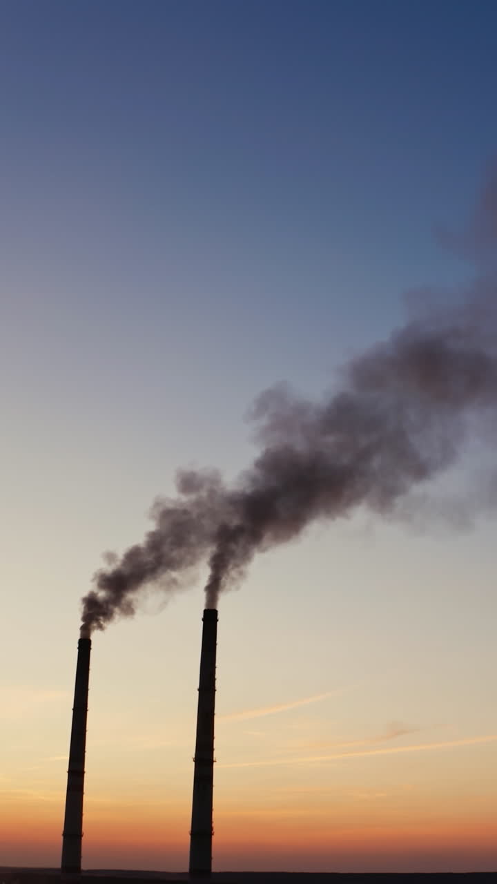 Pollution of the environment.Toxic smoke going from two pipes of a factory on the evening sky background at sunset. Vertical video