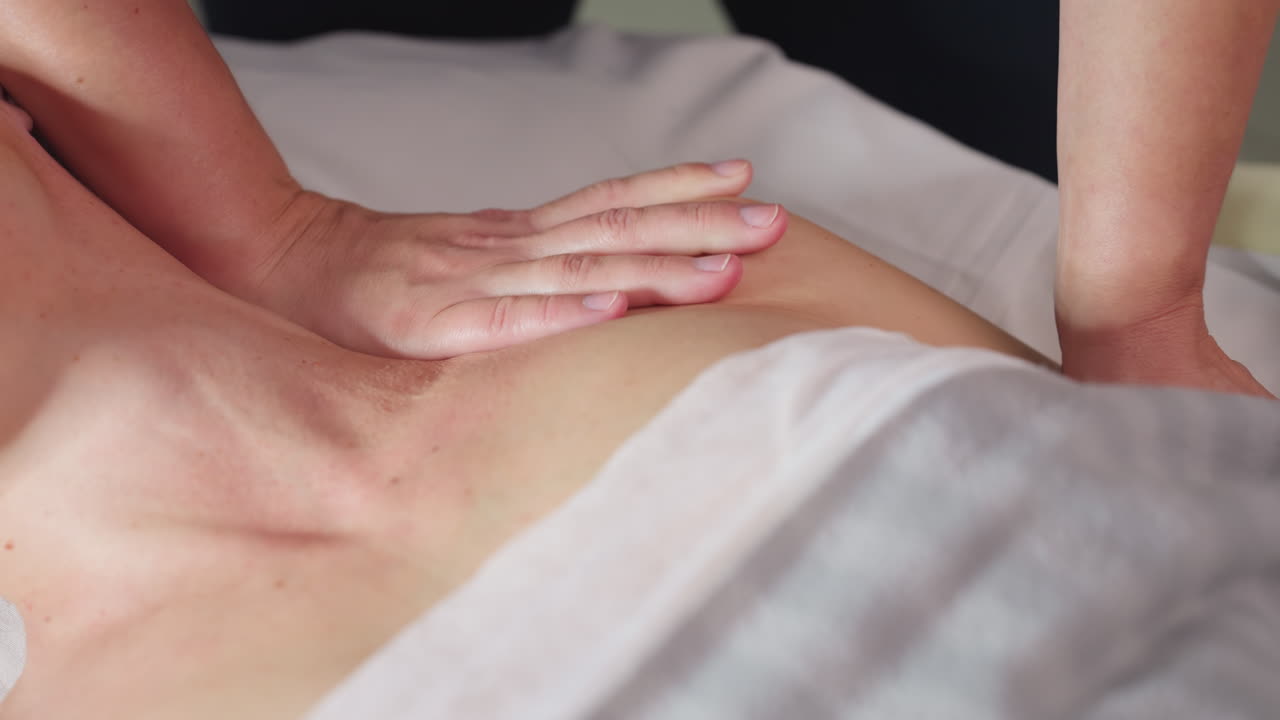 Side view of spa visitor smiling eyes closed as wellness technician works gliding fingertips from side of neck to shoulder delivering soothing massage in bright clean spa environment