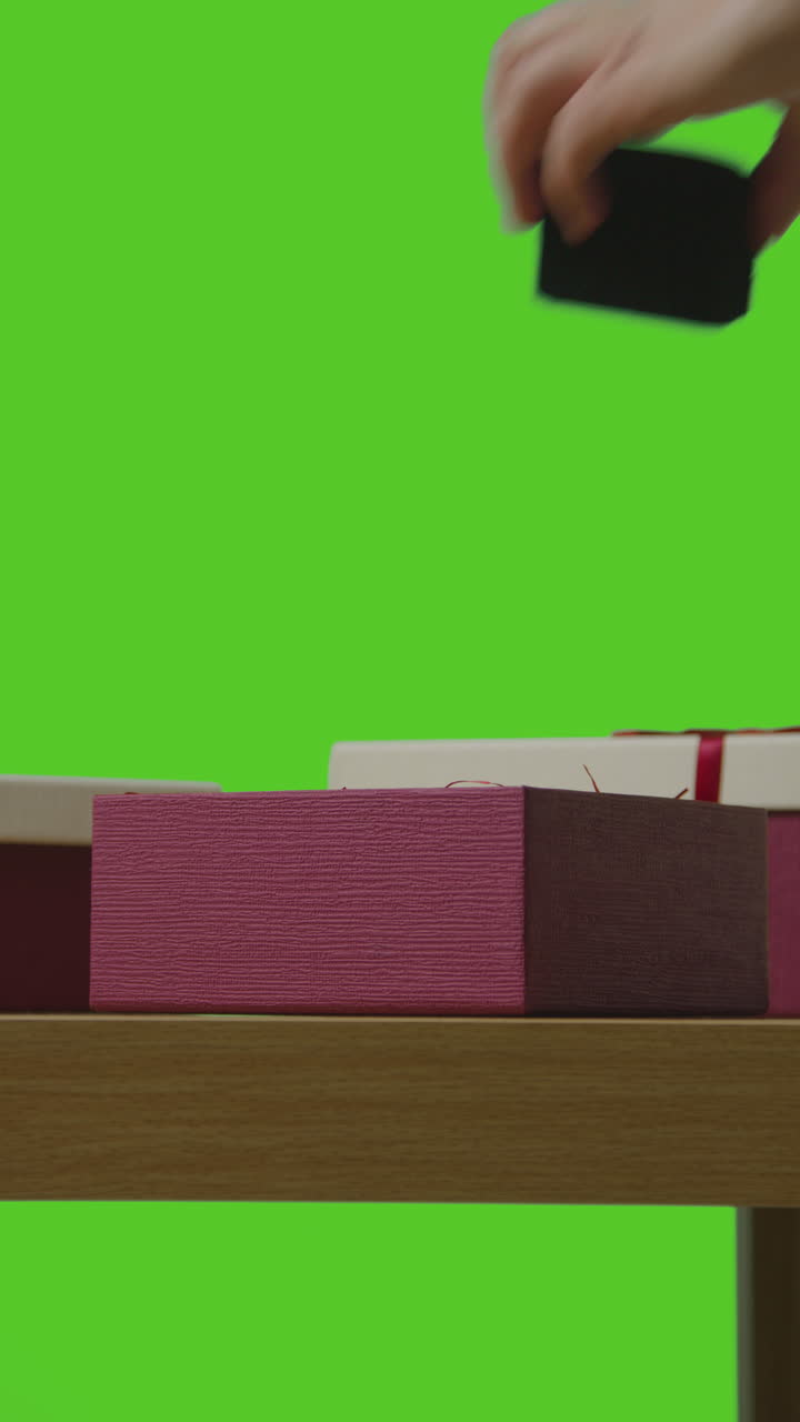 Vertical Video Of Man Putting Present Into Gift Wrapped Box On Table Shot Against Green Screen 1