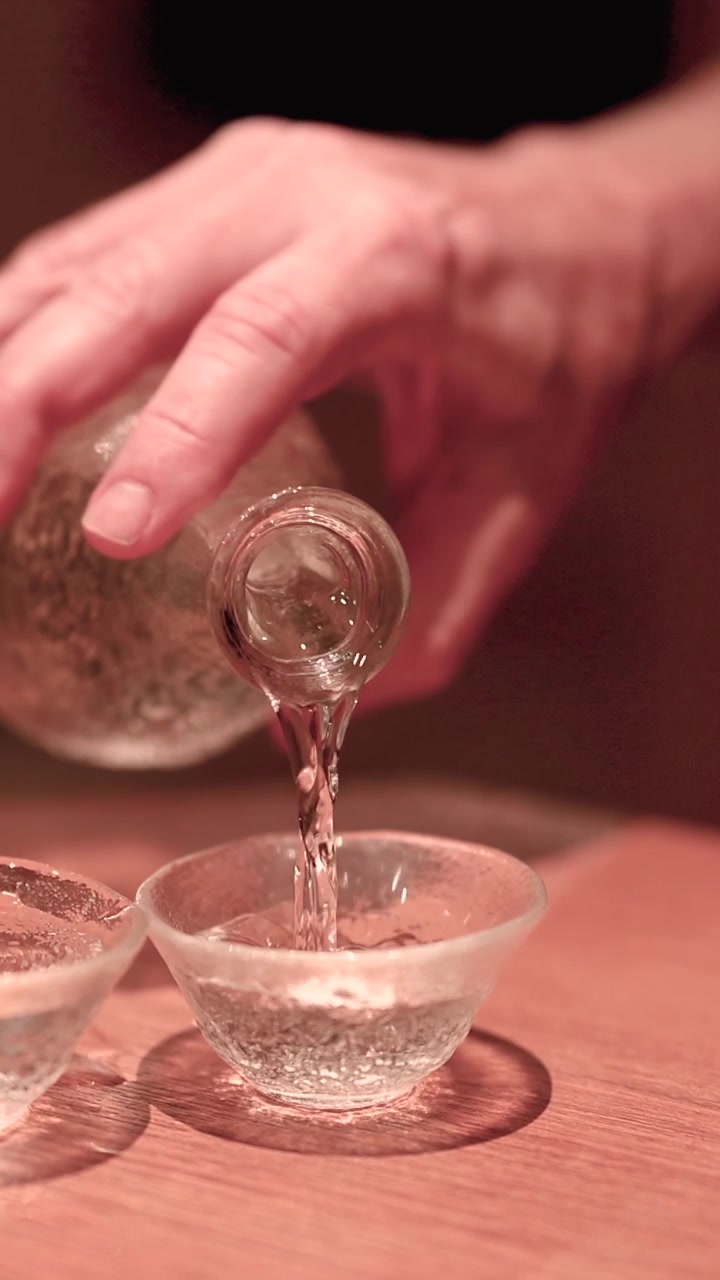 Close-up Tangan Menuangkan Sake ke dalam Gelas Kaca Tradisional