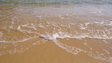 slow motion view of gently clear water waves and sea foam rolling into a beach sand