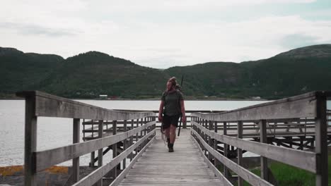 Backpacker-With-Alaskan-Malamute-Dog-Walking-On-Wooden-Platform-Jetty