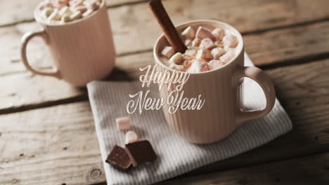 happy new year text over mugs of seasonal hot chocolate with marshmallows on wood background