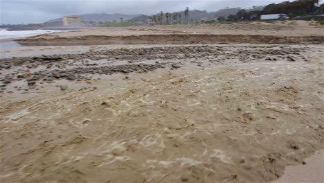 Schwenkaufnahme-Von-Sanjon-Creek,-Die-Nach-Starkem-Regen-In-Ventura-Kalifornien-Strandsand-In-Den-Ozean-Spült