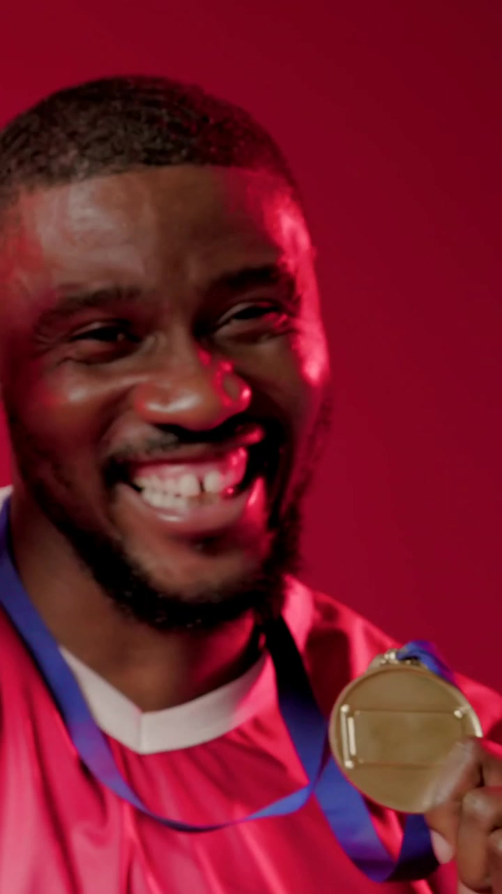 Video verticale: Uomo che riceve una medaglia, solleva una medaglia d'oro con nastro blu in studio, indossando una maglia rossa.